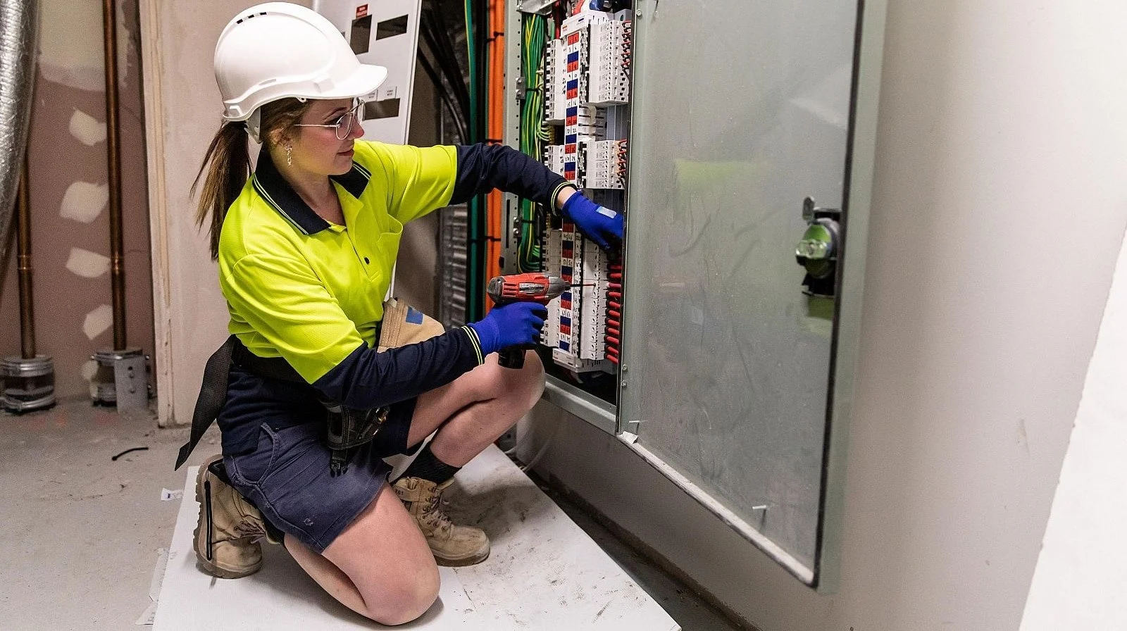 Técnico electricista profesional realizando trabajos de instalación y mantenimiento en un cuadro eléctrico industrial, utilizando herramientas especializadas y equipos de protección.
