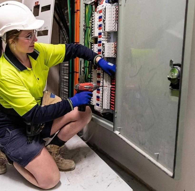 Técnico electricista profesional realizando trabajos de instalación y mantenimiento en un cuadro eléctrico industrial, utilizando herramientas especializadas y equipos de protección.
